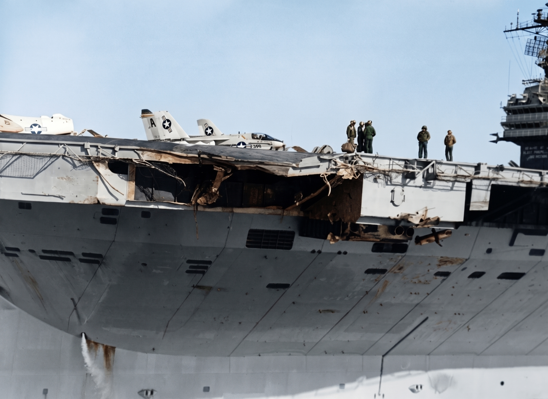USS John F. Kennedy (CV-67) showing the torn and gouged port-side flight deck overhang after the collision with USS Belknap, with crewmen surveying the damage.